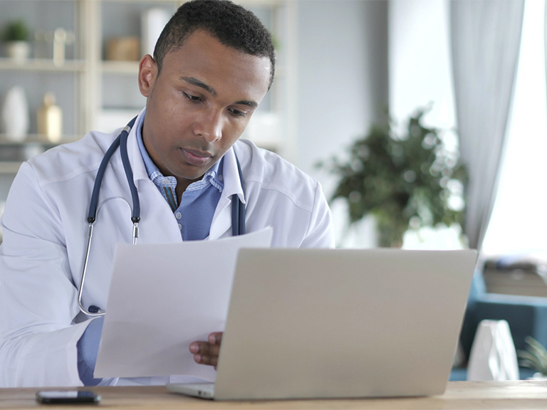 Doctor sitting at a laptop looking over papers.