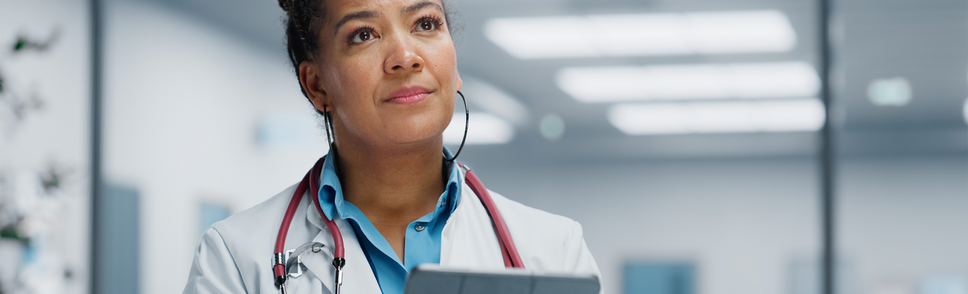 Doctor holding a tablet, looking off into the distance in thought.