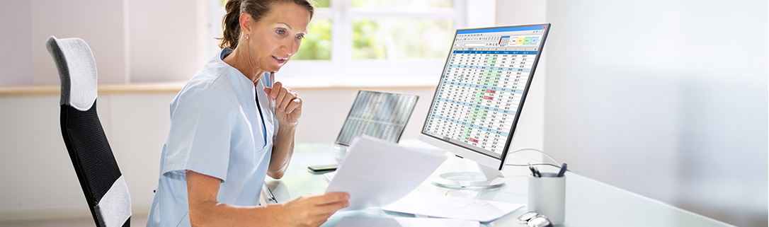 Female doctor looking at papers while sitting at a computer.