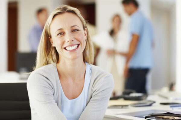 Portrait of cheerful business woman smiling with associates discussing in background.