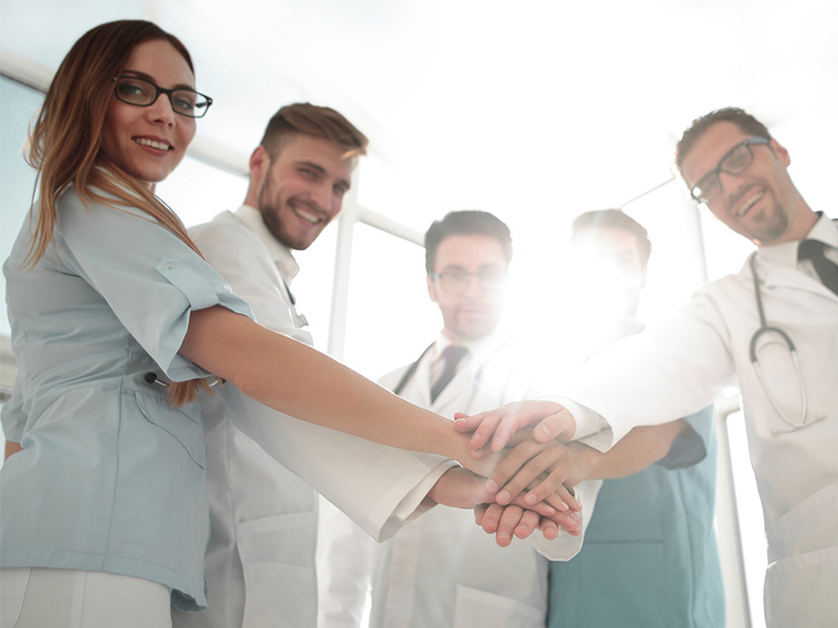 Five doctors smiling and putting their hands together as a team.