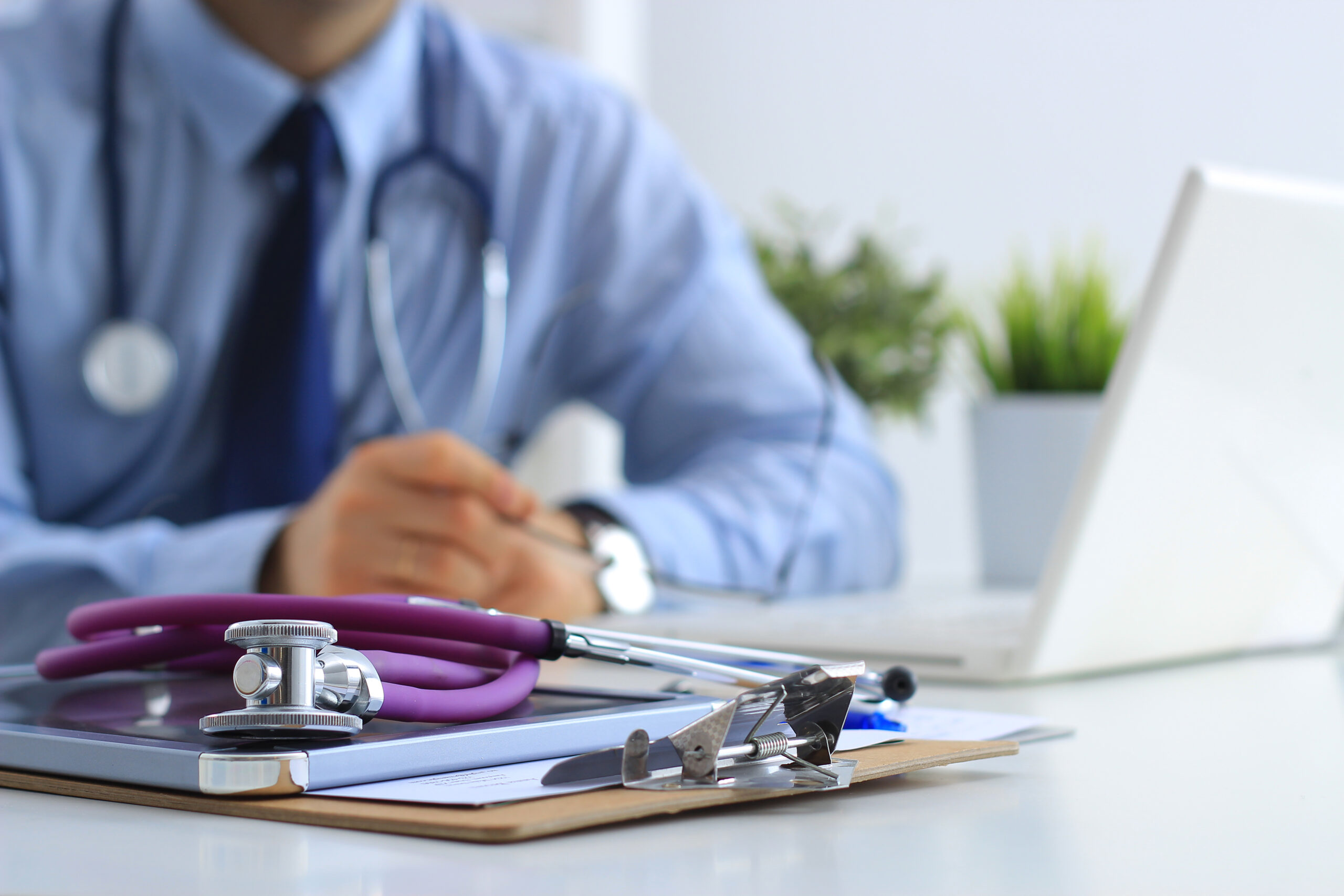 Doctor working on a laptop with medical tools and papers on the desk with him.