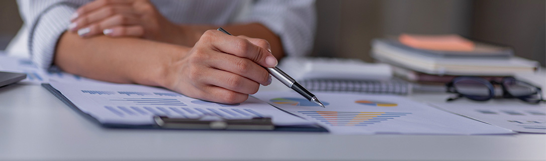 Hands on a desk with a pen, over top of charts.