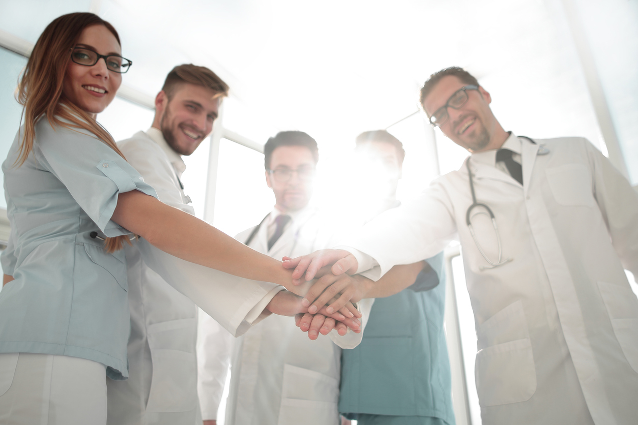 Doctors and nurses coordinate hands in a group circle.