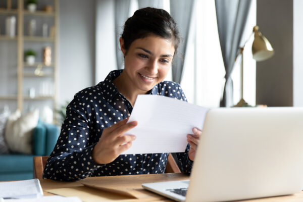 Smiling woman holding reading paper letter sit at table
