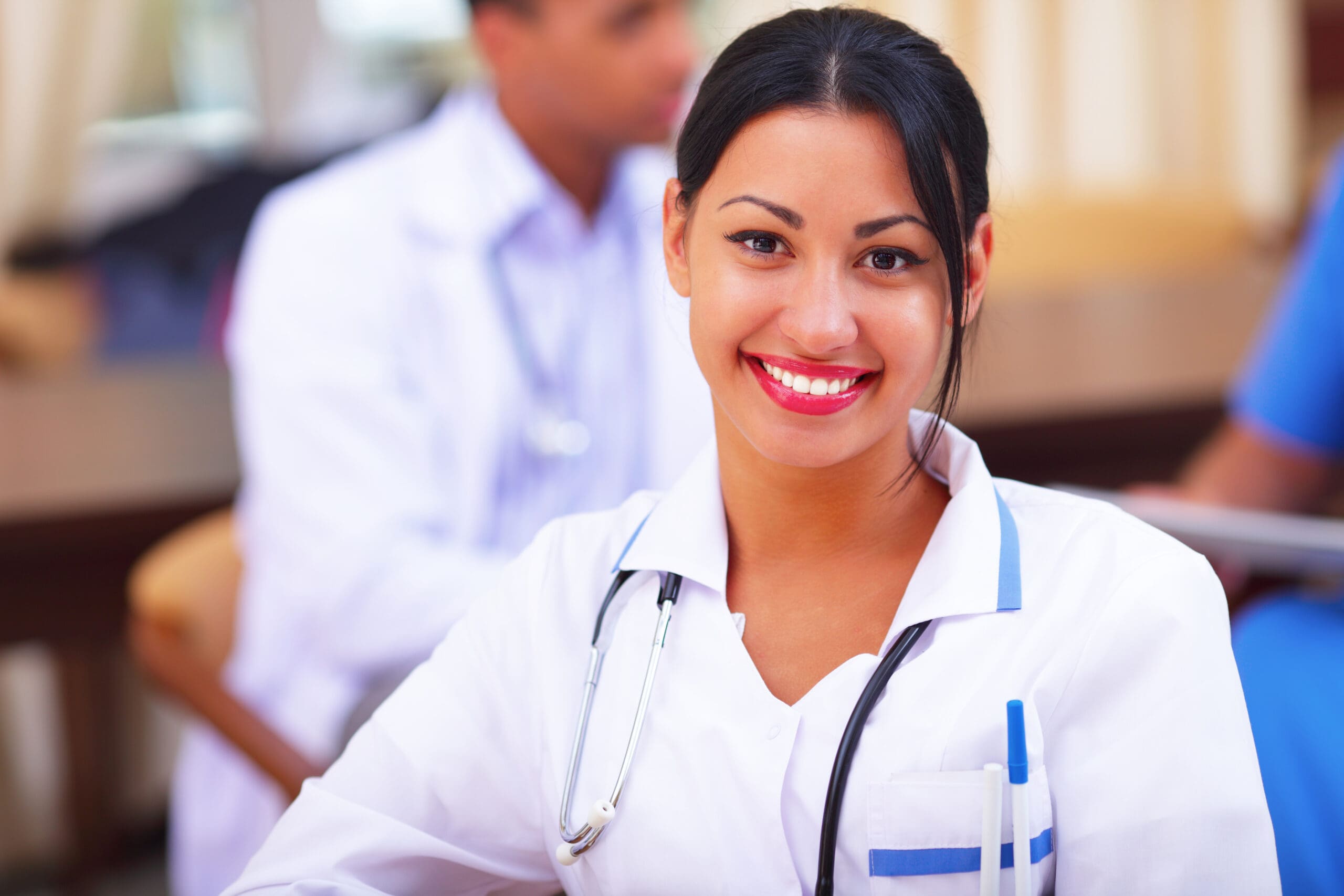 Medical doctor woman smiling indoors with her colleagues working behind