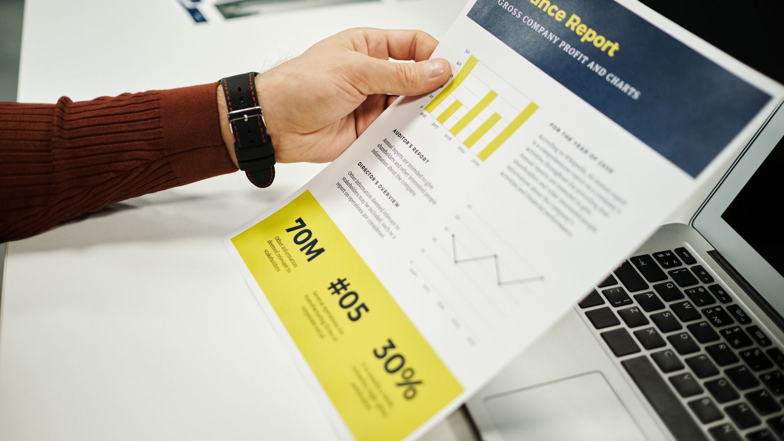 Hand holding a finance report with charts beside a laptop, representing oversight of outsourced medical billing