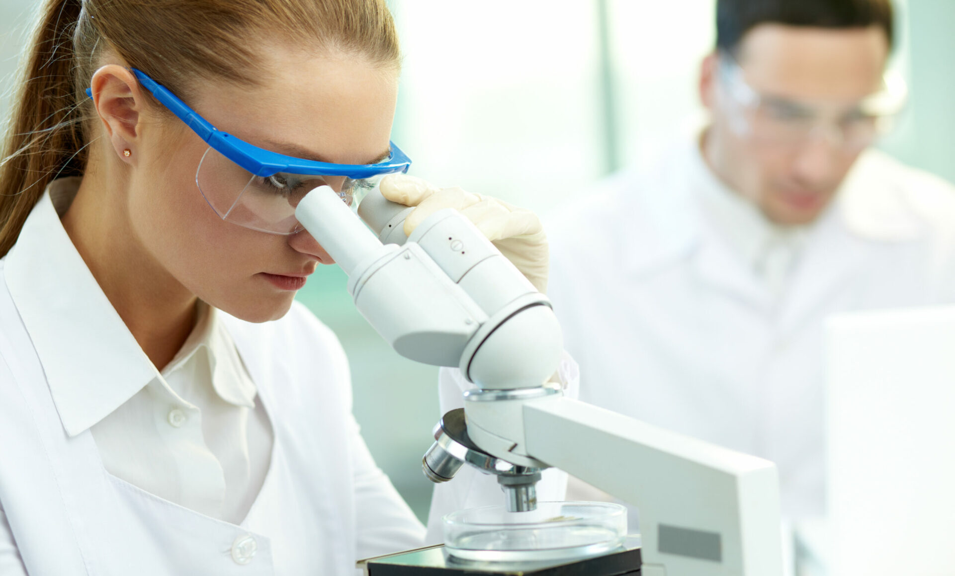 a woman looking through a microscope with a man behind her