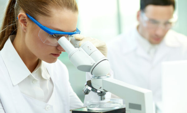 a woman looking through a microscope with a man behind her
