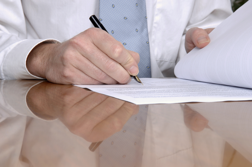 Contract on a desk being signed with a pen.