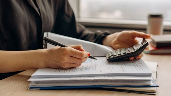 A person reviewing financial documents with a calculator at an office desk, representing rising overhead costs in a medical practice
