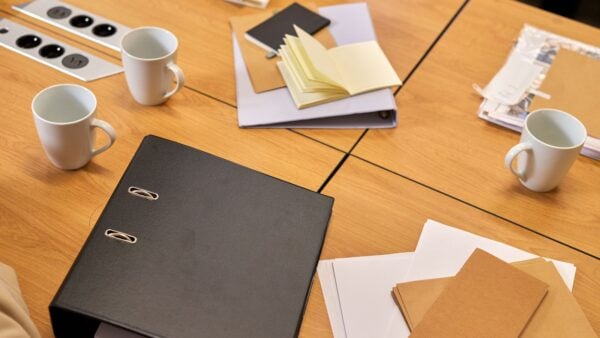 A black policy binder, notepad and documents on a meeting table, representing an employee handbook review