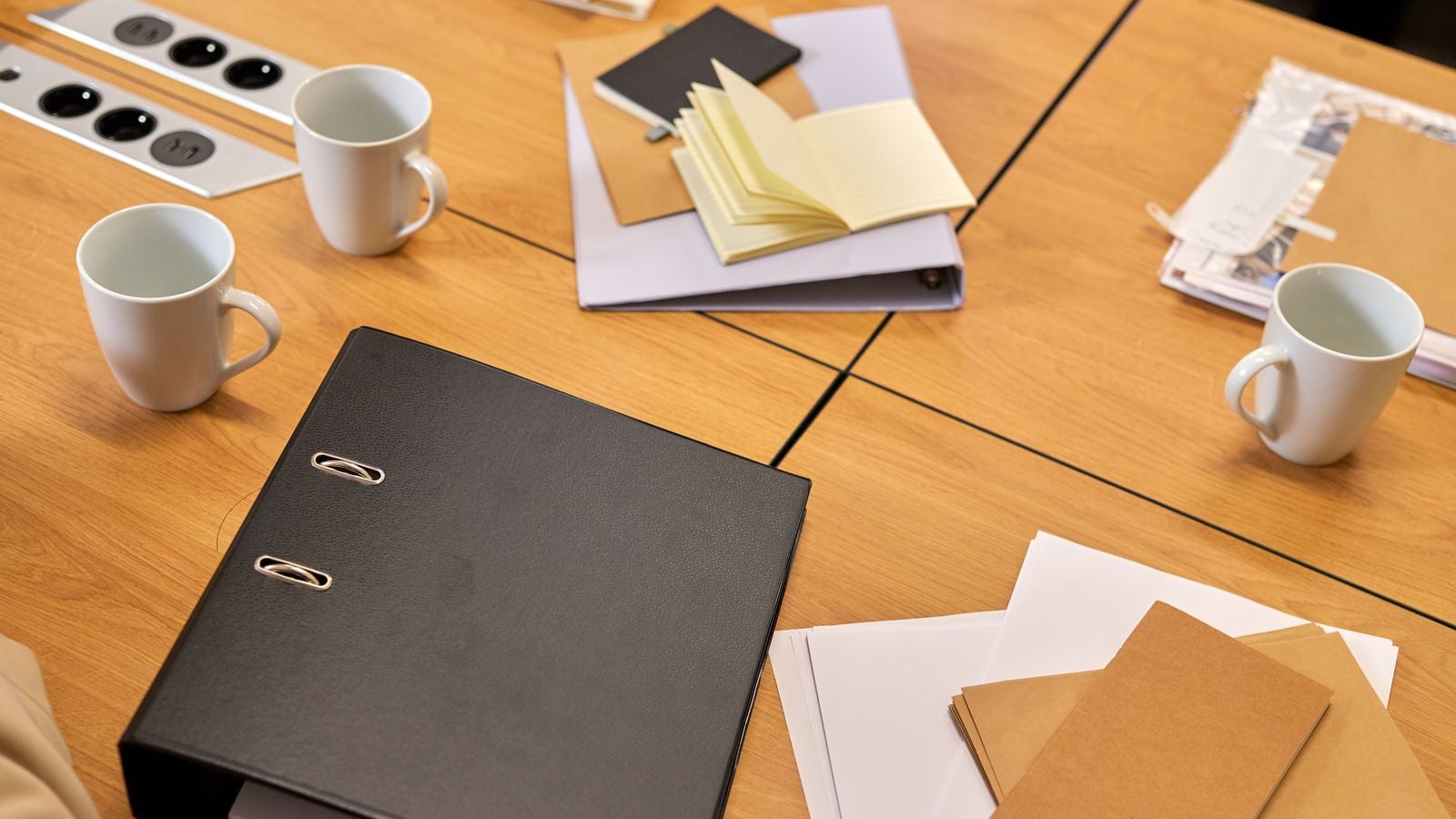 A black policy binder, notepad and documents on a meeting table, representing an employee handbook review